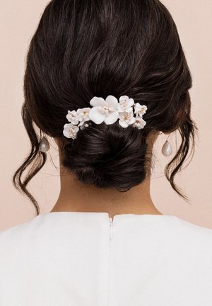 Accessorio per capelli floreale bianco con petali testurizzati e piccole perle, posizionato su un'acconciatura a basso chignon su uno sfondo chiaro.