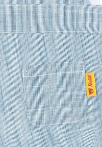 Gestreepte blauwe stof met een patchzak en gele label. De textuur is glad; de strepen zijn smal en gelijkmatig verdeeld.