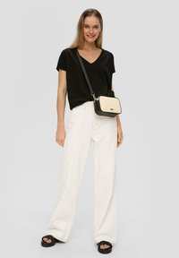 Czarna bluzka z dekoltem w serek, białe spodnie o szerokich nogawkach z widocznym przeszyciem oraz mała czarna i beżowa torba na ramię. Na stopach solidne czarne sandały.