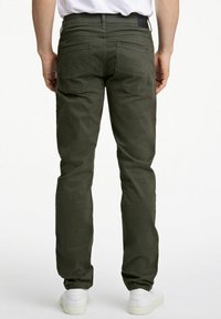 Donkergroene katoen broek met een recht model, twee achterzakken en gedragen met witte sneakers.