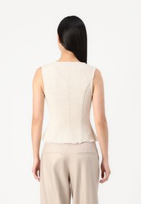 Beige, ärmlös peplumtop med en texturerad yta och fransad nederkant, ihop med ljusa, löst sittande byxor.