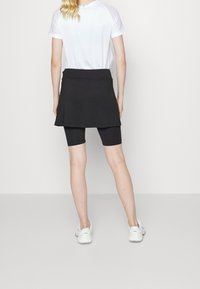 Falda corta deportiva negra sobre unos pantalones cortos de ciclismo negros, combinada con una camiseta blanca de manga corta. Los zapatos son blancos con un logo en la parte de atrás.