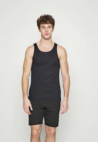 Schwarzes Baumwolltanktop mit breiten Trägern, figurbetontem Design und glatter Textur, kombiniert mit dunklen Shorts. Schlicher, lässiger Stil ohne Muster.