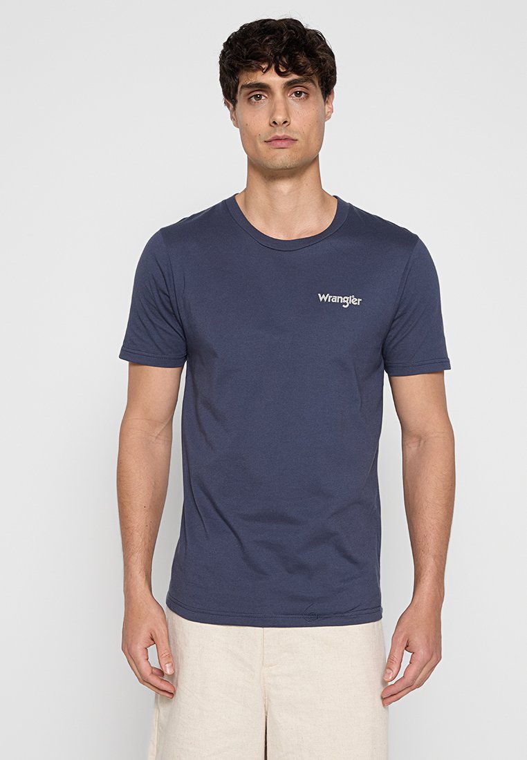 T-shirt in cotone blu navy con collo rotondo, maniche corte e logo bianco "Wrangler" sul petto. Texture liscia e design aderente.