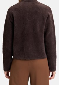 Brown fleece jacket with a textured, soft surface and a high collar; cropped design with dropped shoulders and a relaxed fit.