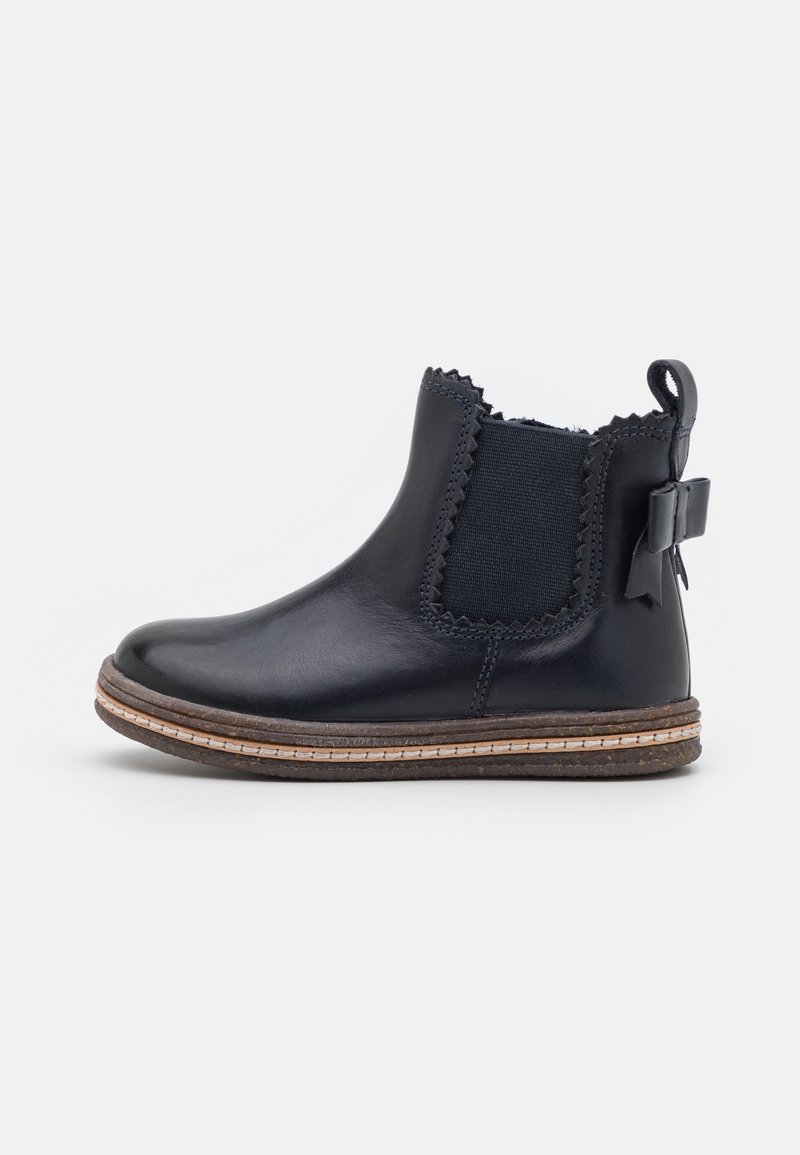 Bottine en cuir noir avec panneau latéral élastique, bords festonnés, semelle marron et nœud décoratif à l'arrière.