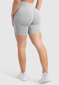 Grijze high-waisted fietsshorts van een textuur met een gladde stof, met een contoured ontwerp voor het verbeteren van de vorm en pasvorm. Witte sportieve sneakers gedragen.