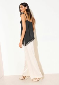 Camisola negra de satén con detalles de encaje en el dobladillo, combinada con pantalones anchos blancos y fluidos y tacones altos nude. Textura suave, diseño minimalista.