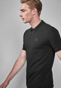 Sort polo skjorte i blødt stof, med en tre-knaps stolpe, korte ærmer, diskret logo detalje og en tætsiddende pasform.