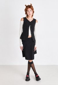 Black vest with buttons, white textured long-sleeve top, black skirt with pleats, sheer black stockings, and platform shoes with red lips design.
