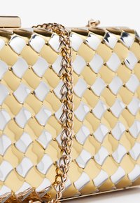 Metallisk clutch-veske med et vevd mønster av gull og sølv. Inkluderer en gullkjede-rem og en klafflås. Glatt tekstur.