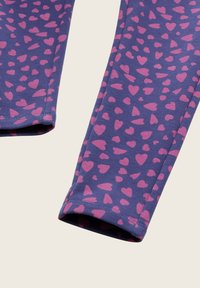 Artimų planų purpurinės medžiagos leggings su rožinėmis širdelėmis ant šviesaus fono.