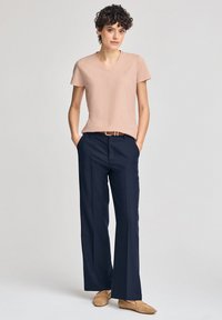 Ljusrosa t-shirt med v-ringning som matchas med marinblå vida byxor, som har ett bälte, samt ljusbruna slipskor mot en neutral bakgrund.