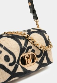 Sac à main texturé en imprimé animal crème et noir, avec une bandoulière en chaîne dorée et un fermoir en logo doré pour une fermeture sécurisée.