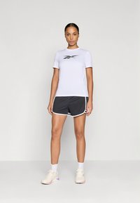 Wit sportief T-shirt met korte mouwen en zwart logo, gecombineerd met zwarte shorts met witte accenten en een losse pasvorm. Lichte sneakers.