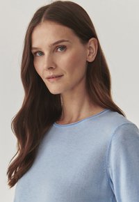 Pulover tricotat de culoare bleu deschis, cu guler rotund și mâneci lungi, având o textură moale și detalii delicate de cusătură.