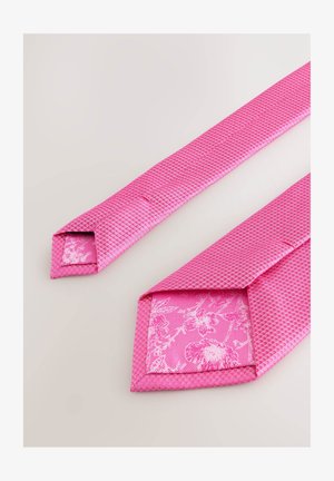 Rožinė kaklavalė su tekstūruotu austiniu raštu. Galinėje dalyje yra kontrastinga gėlėta audinio dalis, kurioje matyti subtilios linijos ir blizgus paviršius.