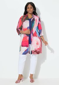 Kolorowa kurtka w stylu kimono z kwiatowymi wzorami w odcieniach różu, niebieskiego i zielonego, noszona na granatowej bluzce, w połączeniu z białymi spodniami i różowymi sandałami.