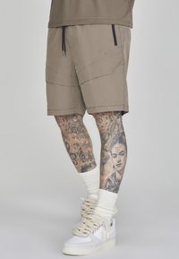 Khakishorts mit elastischem Bund und Kordelzug. Mit schrägen Nähten, zwei Seitentaschen, kombiniert mit weißen Sneakers und Crew-Socken.