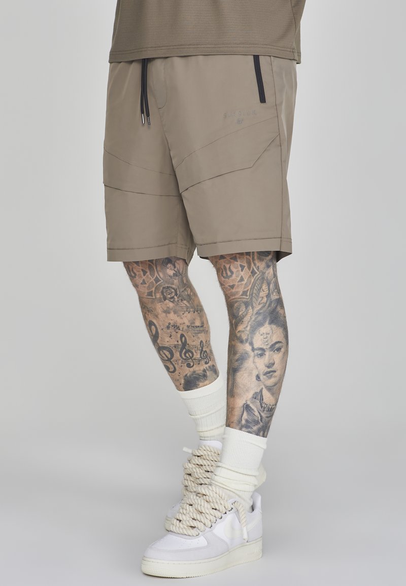 Khakishorts mit elastischem Bund und Kordelzug. Mit schrägen Nähten, zwei Seitentaschen, kombiniert mit weißen Sneakers und Crew-Socken.