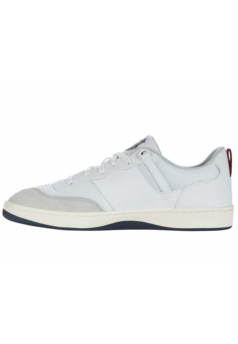 Fehér sneaker szürke velúr részletekkel, sima bőrrel és hálós panelekből. Kerek orral, lapos talppal és piros sarkú füllel rendelkezik.