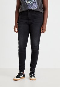 Črne visoko pasne skinny jeans hlače iz denima, z gladko teksturo in ožjim krojem, v kombinaciji s črnimi in belimi supergami z gumijastimi podplati.