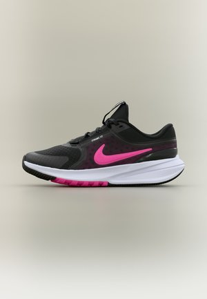 Mustade ja roosade Nike jooksujalatsite valge tallaga, "Dynamic Fit" sildiga ning roosa Nike swoosh-logoga külgedel.