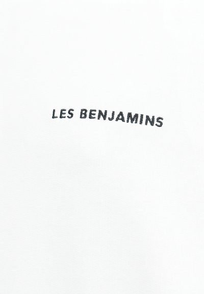 Λευκό ύφασμα με μαύρο κεντημένο κείμενο "LES BENJAMINS" στο κέντρο της επάνω περιοχής.
