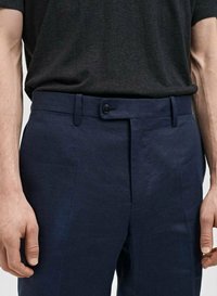 Pantalon bleu marine avec une texture lisse, doté d'une fermeture à bouton, de passants de ceinture et d'un design à devant plat. Porté avec un t-shirt noir.