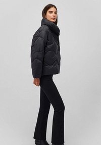Giacca a vento nera con collo alto, caratterizzata da un design trapuntato e da motivi arrotondati. Abbinata a pantaloni neri a palazzo e stivaletti.