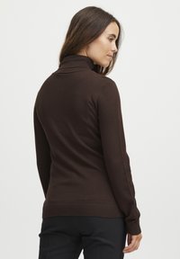 Pruun turtleneck-svellar, mis on valmistatud kerge kangast, millel on istuv disain, soonikkoes olevad varrukad ja sile tekstuur ilma kaunistusteta.