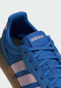 Plava sportska cipela s glatkim kožnim gornjištem, ružičastim detaljima, dizajnom s tri pruge i teksturiranim vezicama. Bijela potplata upotpunjuje izgled.