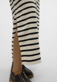 Jupe tricotée rayée en crème et noir, avec une fente sur le côté. Portée avec des chaussures à lacets marron foncé à semelle texturée.