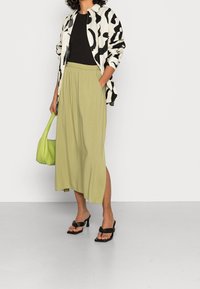 Gestreept zwart-wit shirt, geribbelde zwarte top, vloeiende olijfgroene rok, groene handtas, zwarte hoge hakken; gladde texturen, casual ontwerp.