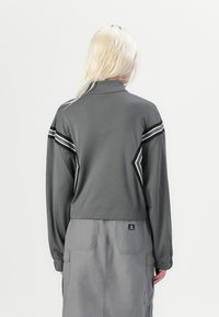 Veste zippée grise avec un col monté, des manches longues et des accents de rayures contrastantes noir et blanc au dos et sur les épaules.