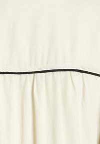 Tecido de cor creme com uma superfície suave e texturizada. Apresenta uma costura horizontal com acabamento em preto, criando um efeito de camadas.