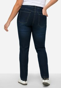 Tmavomodré džínsy s úzkym strihom. Majú dve zadné vrecká, kontrastné prešívanie a stredne vysoký pás. Kombinované s bielymi teniskami.