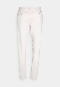 Pantalones ajustados color blanco roto con dos bolsillos traseros abotonados, trabillas para cinturón y corte recto, mostrados desde atrás.