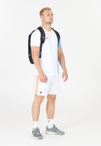 Camiseta blanca con mangas azules, pantalones cortos blancos con franja naranja, zapatillas grises y mochila negra con logo. Diseño de ropa deportiva casual.