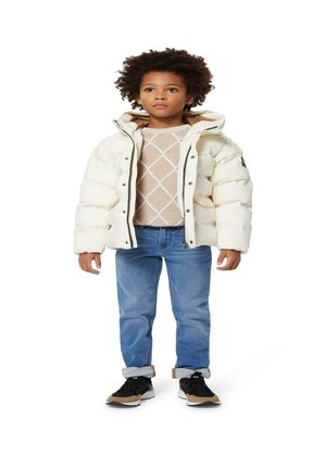Veste blanche duvetée avec capuche, pull en tricot beige avec un motif en losange, jean bleu et baskets noires avec accents bruns.