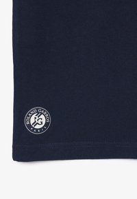 Tissu bleu foncé avec un petit logo circulaire blanc Roland Garros Paris près du bord inférieur.