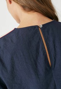 Navyblauwe jurk met een textuur die lijkt op gekreukte stof. Heeft een sleufopening aan de achterkant met een knoopsluiting.
