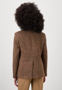 Brun guldspetsblazer med skräddarsydd passform, strukturerat tyg och en enkel vent bak, kombinerad med ljusbruna byxor.