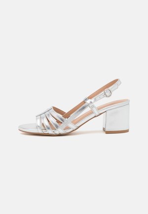 Sølv åben-tå damesandal med blokhæl og justerbar slingback-rem på hvid baggrund.