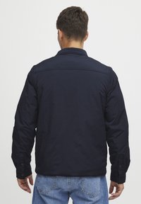 Navy blue jacket featuring a collared design, long sleeves with buttoned cuffs, and a smooth, textured fabric. Back view showing stitching details.