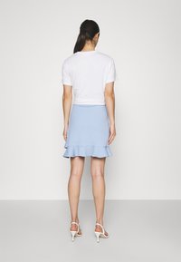 Lichtblauwe geplooide rok met een gelaagde ruchezoom, gecombineerd met een wit cropped t-shirt en witte sandalen met hoge hak.