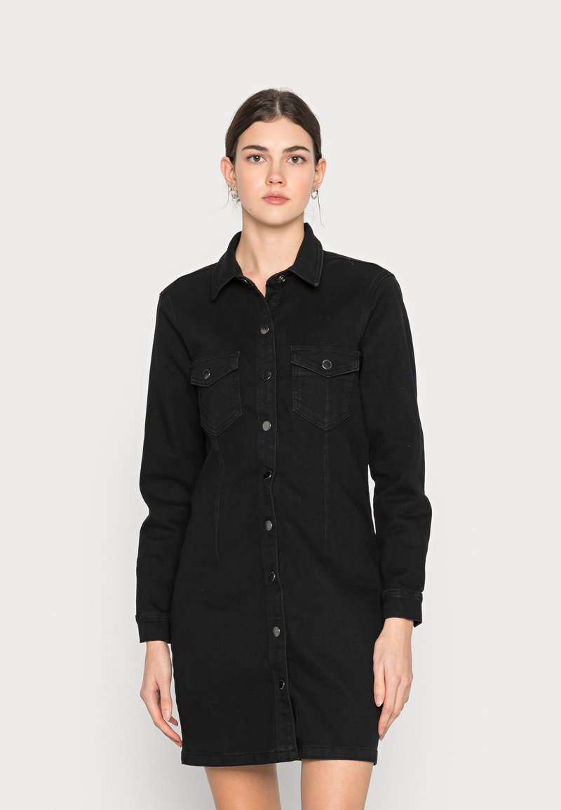 Vestido de camisa em denim preto com fecho frontal de botões, dois bolsos no peito, mangas longas e uma silhueta justa com comprimento até à metade da coxa.
