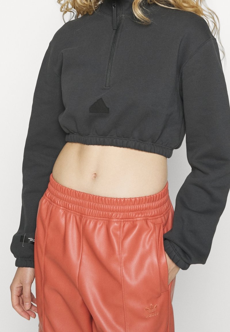 Black cropped sweatshirt with a high collar, featuring a quarter zip and elastic hem. Paired with vibrant orange leather joggers.