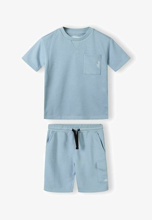 Svijetloplavy pamučni majica s kratkim rukavima i džepom; odgovarajuće kratke hlače s elastičnim pojasom i bočnim džepovima. Meka tekstura.