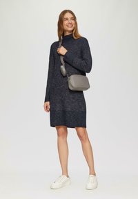 Abito maglione lavorato a maglia blu navy con scollo alto, coste testurizzate e una vestibilità comoda. Abbinato a una borsa a tracolla grigia e sneakers bianche.